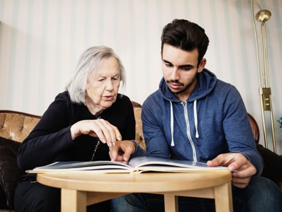 Seniorin und junger Mann schauen Fotoalbum an